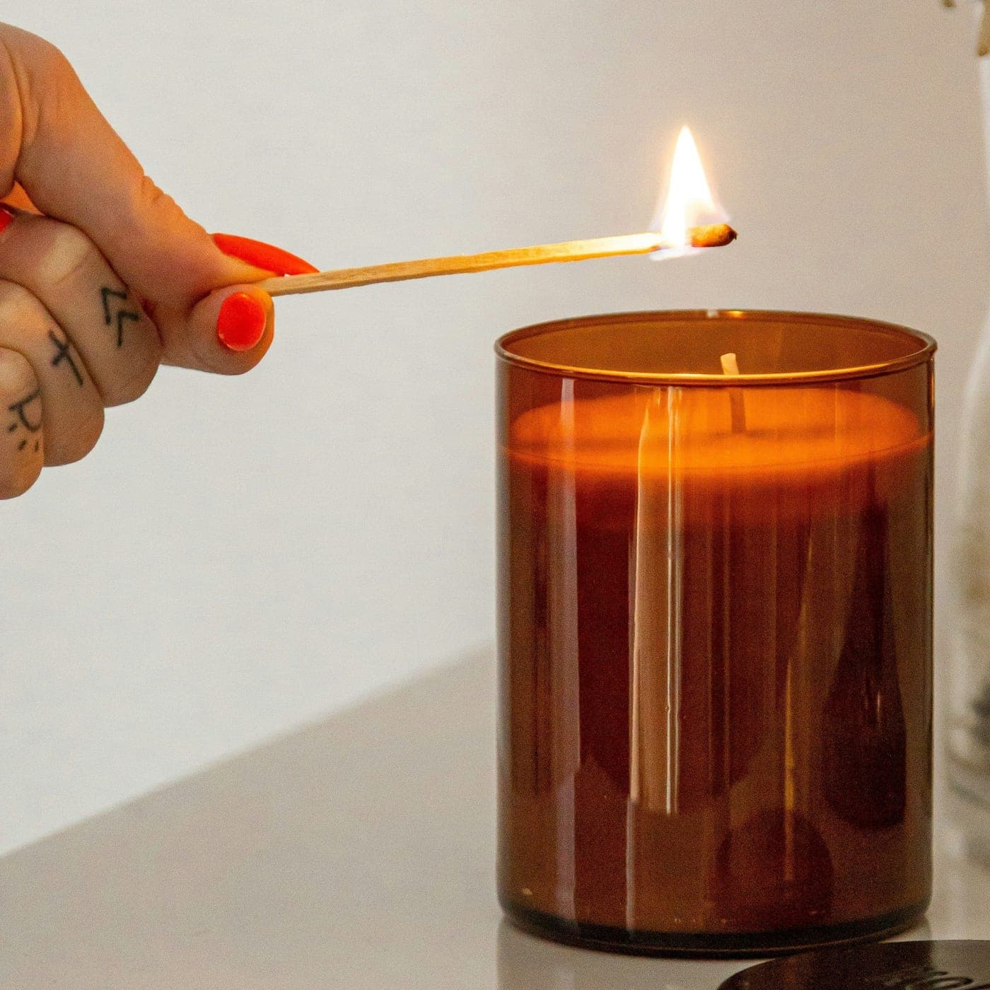 Vanilla Amber Candle — A hand lighting an amber glass jar candle with a long match