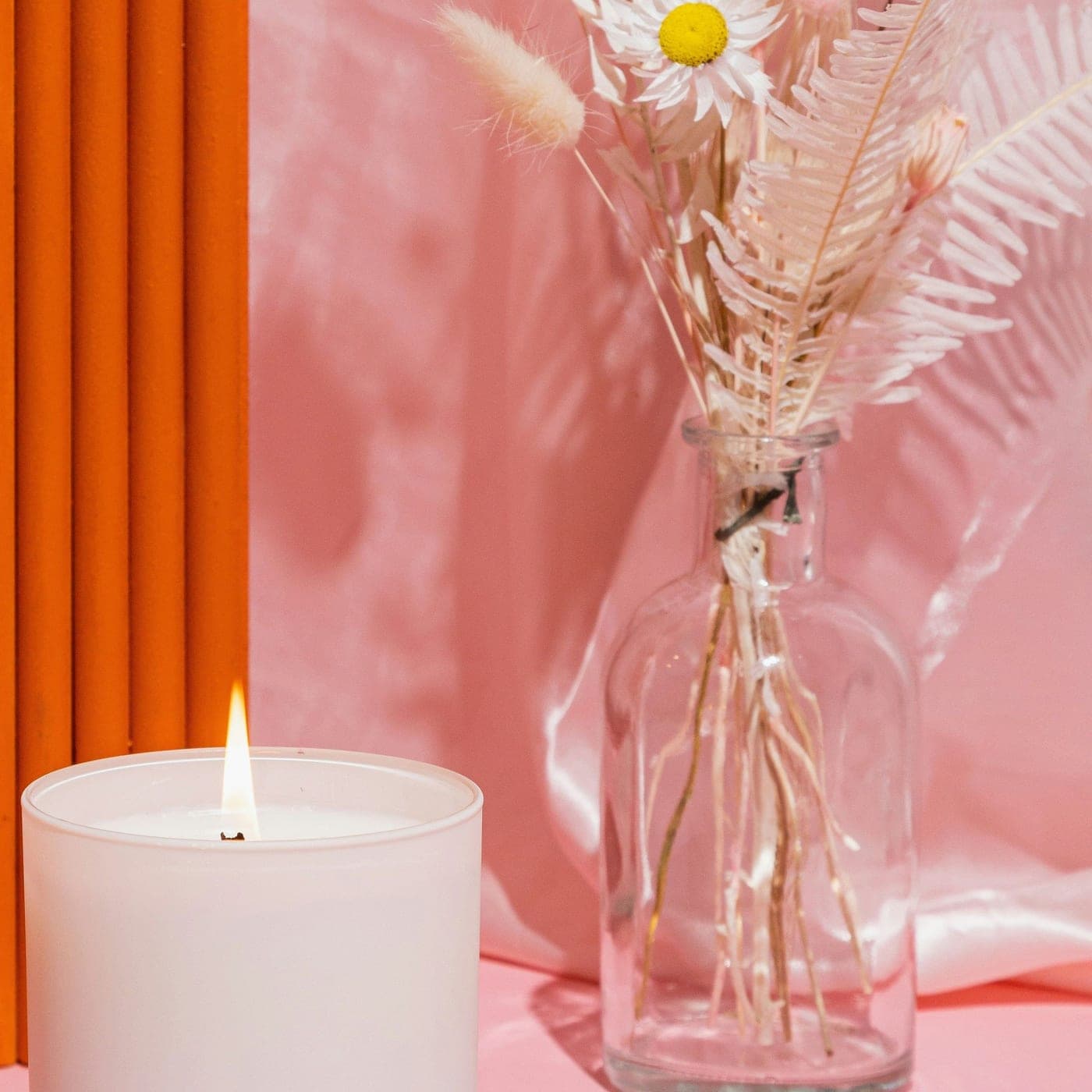 Saffron & Rose Diwali Candle — A lit white candle beside a bouquet of dried flowers on blush silk