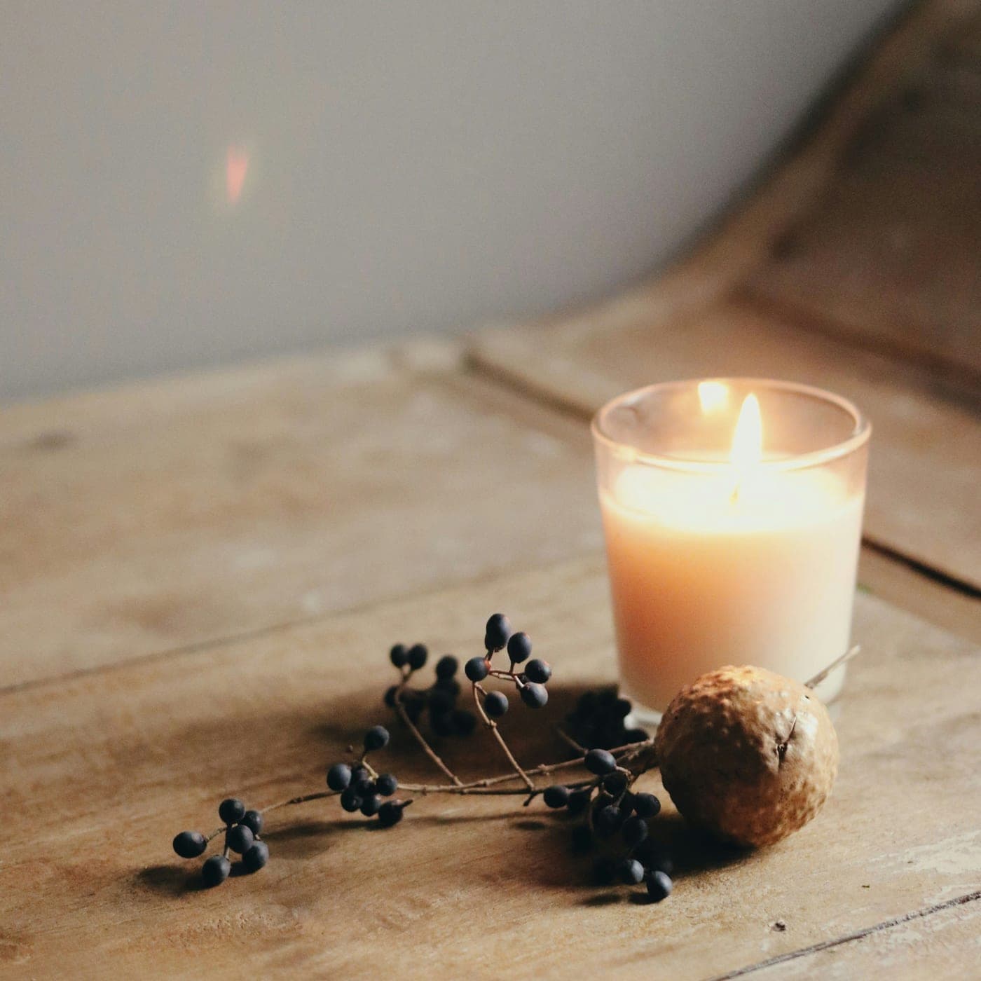 Ocean Breeze Candle — A lit candle in a clear glass votive on weathered wood, with dried berries